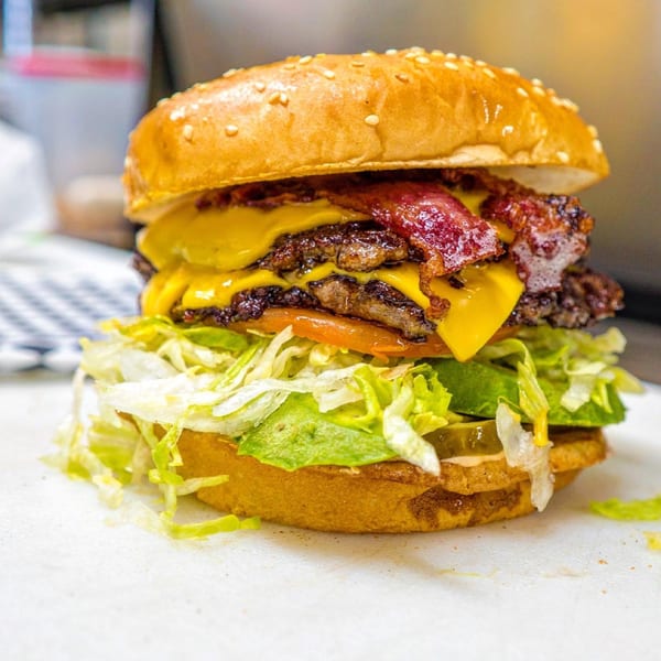 A Frosty King double bacon cheeseburger with lettuce, tomato, and pickles on a sesame seed bun.