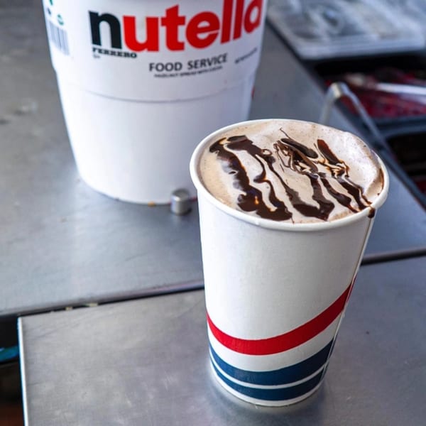 A Nutella-drizzled milkshake in a Frosty King branded cup sits next to a large Nutella container.