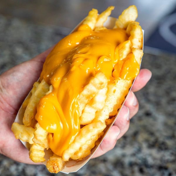 Hand holding a paper tray of Frosty King crinkle-cut fries generously topped with melted cheese sauce.