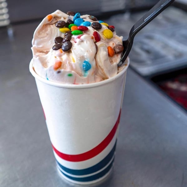 A Frosty King ice cream cup filled with soft serve and colorful M&M's, with a black spoon.
