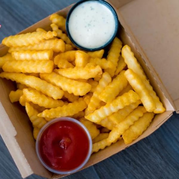 Crispy crinkle-cut fries in a cardboard tray with small cups of ketchup and ranch dressing.